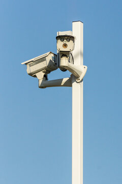 Red-light cameras mounted on a tall post against a blue sky