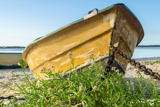 Ground level view of an old row boat chained up on the beach