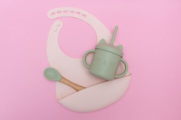 Modern pastel color set of silicone bib cups with straws and spoon on pink background. Baby tableware, first feeding, serving concept.