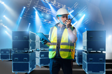 Stage crew manager in safety gear communicates via walkie-talkie and checks equipment with tablet...