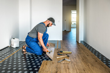 Professional carpenter master worker joining vinyl or laminate floor covering at home renovation. Industrial theme