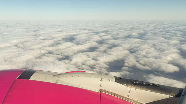 Vibrant pink airplane wing over a vast sea of soft white clouds under a clear blue sky. Captures the serenity and awe of in-flight travel