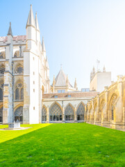 Fototapeta premium Visitors enjoy the serene green lawn at Westminster Abbey's cloisters on a bright day. The historic architecture stands proudly against the clear blue sky, creating a peaceful atmosphere.