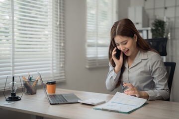 Obraz premium Young professional managing her business from her modern office, reviewing reports and discussing strategies on a phone call, demonstrating efficiency and multitasking skills