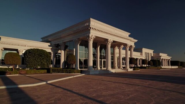 Elegant Estate's Grand Facade: An expansive and stately mansion, showcasing a pristine architectural design with classical pillars and sophisticated details, bathed in the warm glow of sunlight.