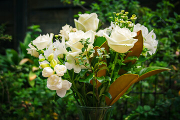 A lush bouquet of fresh white roses and delicate blooms arranged in a glass vase, set against a vibrant green garden backdrop. Perfect for weddings, sympathy, or elegant home decor inspiration