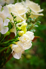 Close up of a lush bouquet of fresh white roses and delicate blooms arranged in a glass vase, set against a vibrant green garden backdrop. Weddings, sympathy, or elegant home decor inspiration