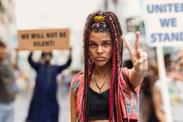 Young mixed-race woman in crowd leading peace protest by making victory sign