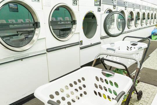 A row of tumble dryers in a launderette with washing carts in front