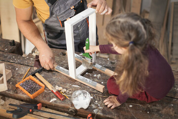 Father and daughther painting wooden frame in workshop