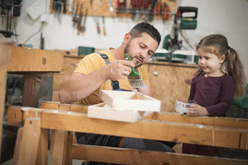 Father and daughther painting wooden frame in workshop