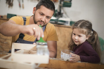Father and daughther painting wooden frame in workshop