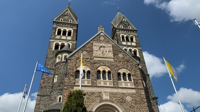 Front facade of Church of Saint Come and Damien. This romanesque style church is located at Clervaux town centre. The EU and Luxembourg flags are waving in front. Clervaux, Luxembourg