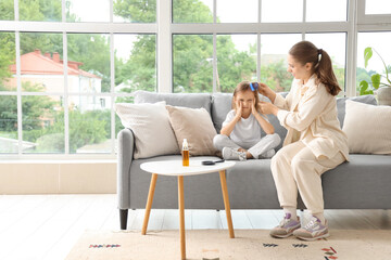 Mother combing her little daughter's hair with pediculosis on sofa at home