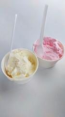 Two different flavours of cold ice cream in paper cups, one strawberry flavour  and one vanilla flavour.