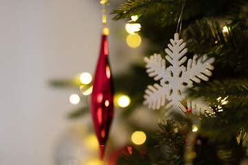 Close-up of red Christmas ornament and snowflake decoration on a decorated tree with warm lights.