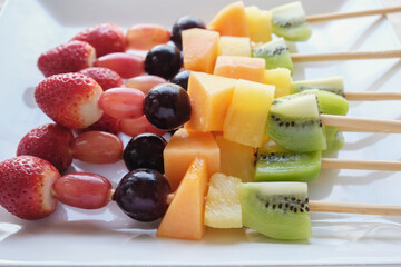 Fresh rainbow fruit skewers on white plate