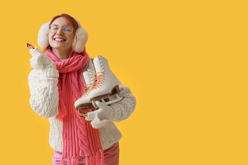 Beautiful young happy woman with ice skates on yellow background