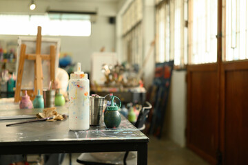 Close-up of colorful paint bottles and tools on a splattered table in a bright art studio