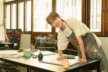 Cheerful art teacher smiling while working with paint and canvas in a bright studio. Engaged in creative work, surrounded by art tools, expressing joy through hands-on teaching
