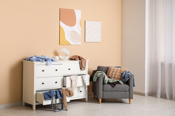 Interior of messy living room with armchair, commode and different scattered clothes