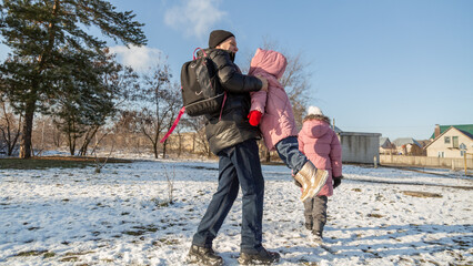 Grandfather walks with his granddaughters after school in the park in sunny winter day