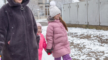 Grandmother and girls walk along a snowy street in winter