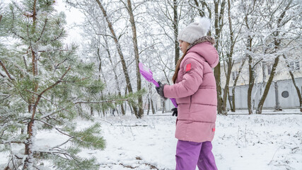 Small girl playing with snow. Child in winter forest on snowy cold day.