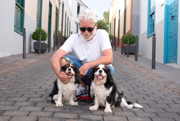 Smiling senior man on the pedestrian street with his two Cavalier King Charles Spaniel dogs. Attractive bearded senior man outdoors with his best animal friends, pet therapy concept.