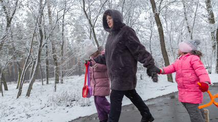 Grandmother with grandchildren in warm clothes playing outdoors in winter park, enjoying snowy...