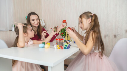 Mother and her daughter painting eggs. Happy family preparing for Easter. Cute little child girl wearing bunny ears.