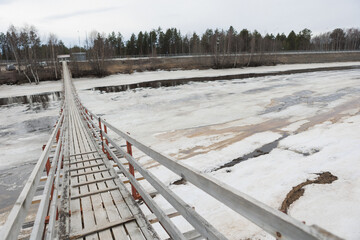 A wooden bridge spans a tranquil water body, surrounded by snow