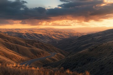 Naklejka premium A remote mountain pass under a dramatic sunset sky, road winding through golden-lit slopes