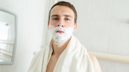 Young man applying shaving foam near mirror in bathroom
