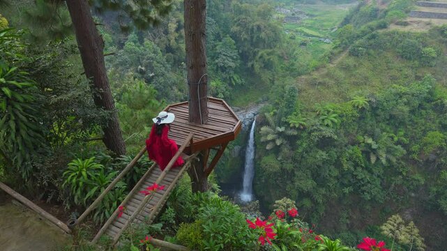 Female tourist walks on wooden bridge at the viewpoint of Air Terjun Kedung Kayang Waterfall, Indonesia.