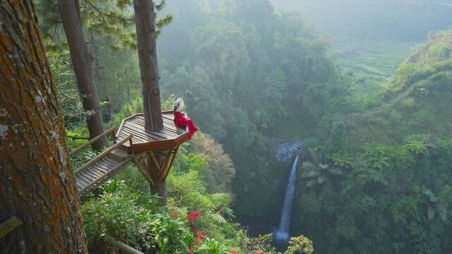 Female tourist  on wooden bridge at the viewpoint of Air Terjun Kedung Kayang Waterfall, Indonesia.