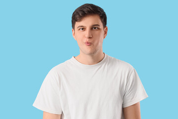 Young man doing face building exercise on blue background
