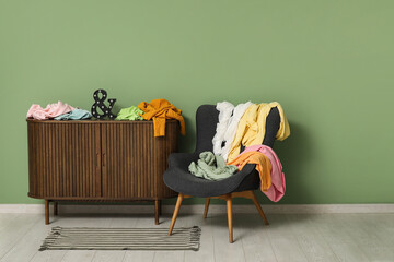 Armchair and commode with scattered clothes near green wall in room