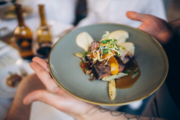 Gourmet beef dish served on a blue plate with vegetables and sauce at a fine dining restaurant during a special dinner event