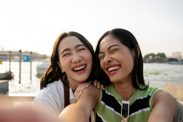 Two happy female friends taking a selfie by the river laughing out loud