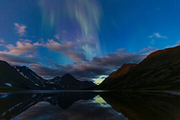 Aurora in the night sky cut the mountains, reflected in the water. Yamal. Russia