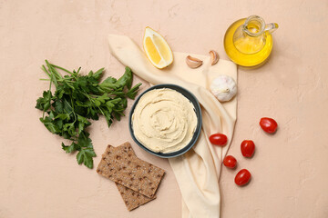 Bowl of tasty hummus with ingredients, crackers and napkin on beige grunge background