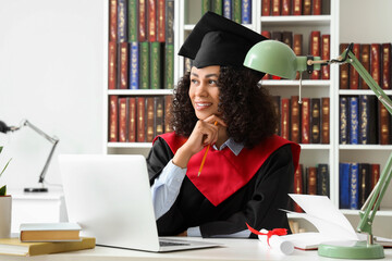 Pretty African-American female graduate with laptop sitting at table in library