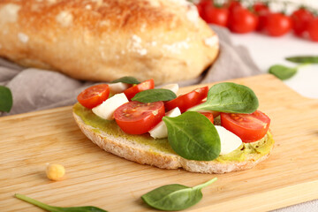 Tasty sandwich with avocado hummus, mozzarella cheese, tomatoes and basil on wooden board, closeup