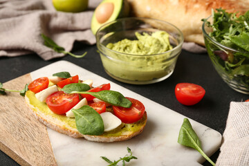 Tasty sandwich with avocado hummus, tomatoes, mozzarella cheese and basil on dark table, closeup