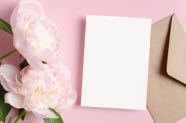 Blank wedding invitation or greeting card mockup with envelope and pink peony flowers, top view, copy space