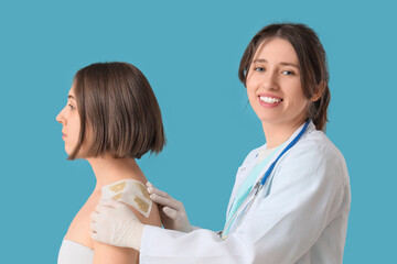 Female doctor applying mustard plaster on patient's shoulder against blue background