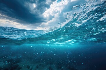Underwater scene of a stormy ocean.  A wave crests and crashes, exposing the deep blue depths below, dotted with bubbles. Dramatic storm clouds are visible above the water's surface