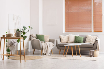 Interior of light living room with sofa, armchair and blinds on window