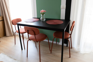 Modern Scandinavian Dining Space with Black Table, Coral Chairs and Green Accent Wall